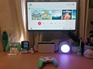 A desk with a monitor and a docked nintendo switch. On the table there is a switch pro controller.
