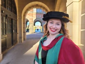Lizzie wearing the University of Birmingham's PhD robes: red and green, with a tudor bonnet hat.