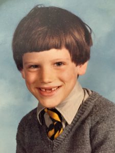 A schoolboy smiling at the camera with bad hair and gappy teeth